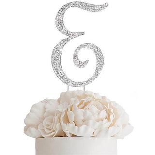 Glittery silver letter "E" cake topper on white peony flowers