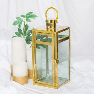 Gold metal lantern with glass panels, surrounded by candles and greenery.