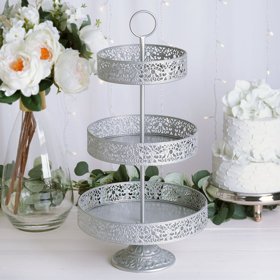 Three-tiered silver serving tray with decorative cutouts in a styled setting.