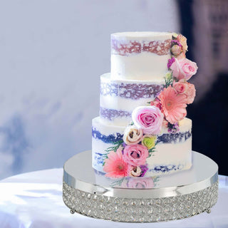Three-tiered wedding cake decorated with pink flowers and a silver cake stand.
