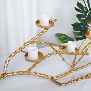 Gold branch candle holder with white candles and green leaves in the background.