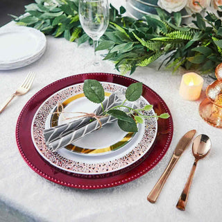 Elegant table setting with burgundy charger plate and decorated napkin.