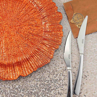 Orange textured plate with silver knives on a sequined surface.