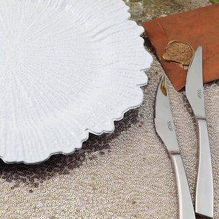 Elegant white serving plate with silver knives on sequined tablecloth.