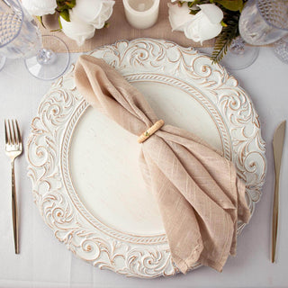 Ornate white dinner plate with a beige napkin and decorative ring
