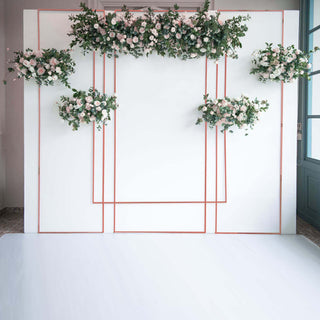 Floral backdrop with pink roses and greenery against a white wall.