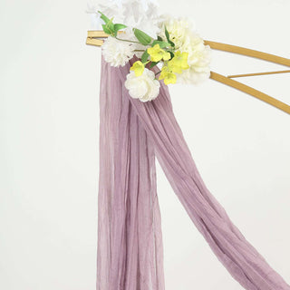 Purple fabric draped elegantly with faux flowers on a gold stand.
