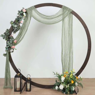 Decorative floral arch with draped fabric and lanterns on a wooden base.