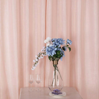 Blue flowers in a vase with two glasses on a marble table against pink curtains.