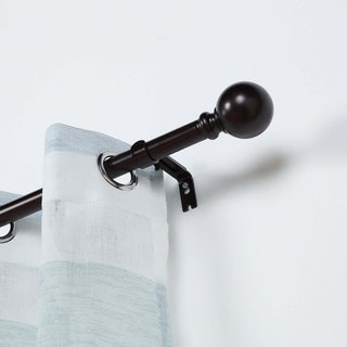 Curtain rod with decorative finial and curtain rings on a plain background
