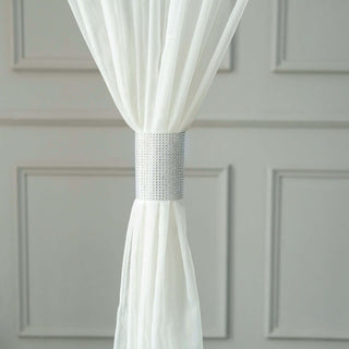 White sheer curtain with silver tieback on a textured wall.