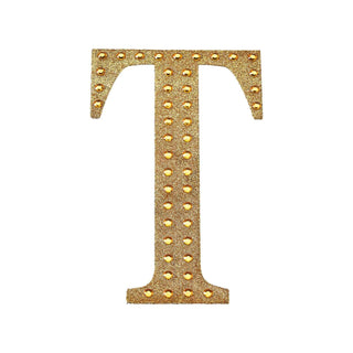 Gold studded letter T on a plain white background