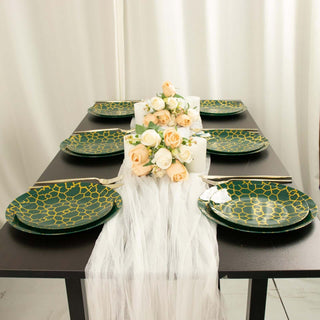Green and gold patterned dinner plates arranged on a black table with floral centerpiece.