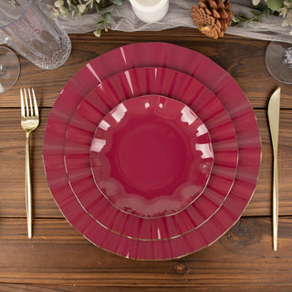 Set of three burgundy plates with gold trim on a rustic wooden table.