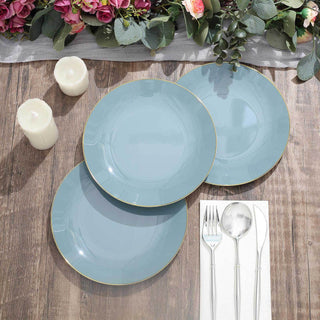 Elegant blue plates with gold rim on a wooden table with candles and floral decor.
