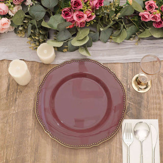 Elegant burgundy dinner plate with gold trim on a rustic wooden table setting.
