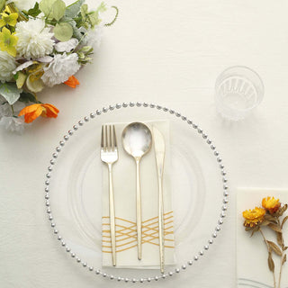 Elegant dining setup with clear plate, gold utensils, and floral decor.