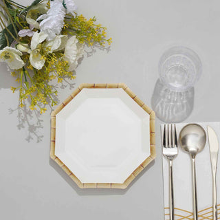 White octagonal plate with bamboo design, silver cutlery, and glass on a gray table.