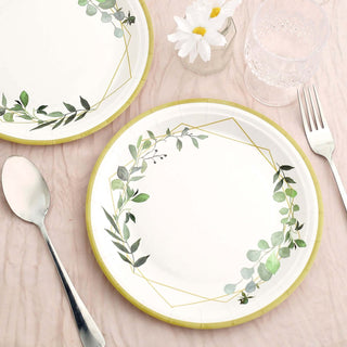 Decorative paper plates with greenery design, set on a table with utensils.