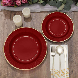 Elegant red dinner plates set with gold trim on a rustic wooden table.