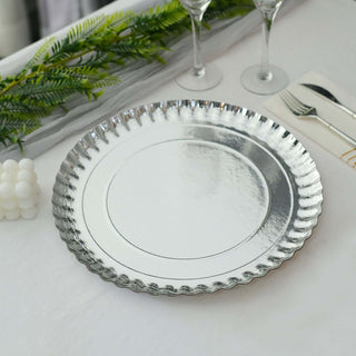 Silver decorative plate on a table with greenery and glassware.