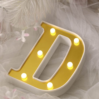 Illuminated letter "D" marquee sign with yellow lights on a soft background.