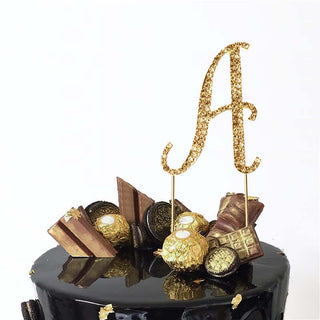 Gold glitter "A" cake topper with decorative elements on a black cake.