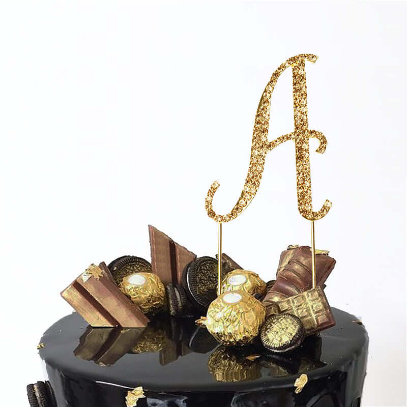 Gold glitter "A" cake topper with decorative elements on a black cake.