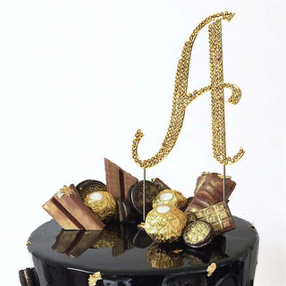 Gold glitter "A" cake topper with decorative elements on a black cake.