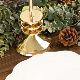 Gold candle holder on a wooden table with greenery and a pinecone.