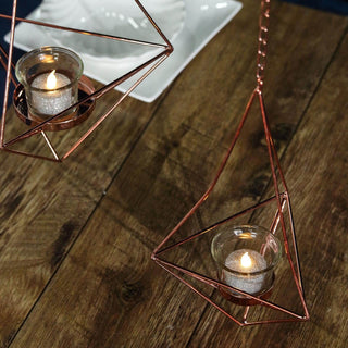 Geometric copper candle holders with glass votives and lit candles.
