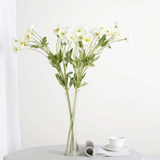 White flowers in a clear vase on a round table with a cup and magazine.