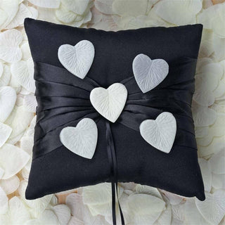 Black decorative pillow with white heart embellishments on a bed of petals.
