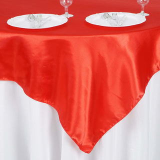 Red satin tablecloth draping over a white table with plates and glassware.