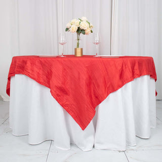 Red tablecloth draped over a round table with wine glasses and flowers.