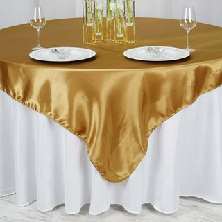 Gold satin tablecloth draped over a round table with plates and glasses.