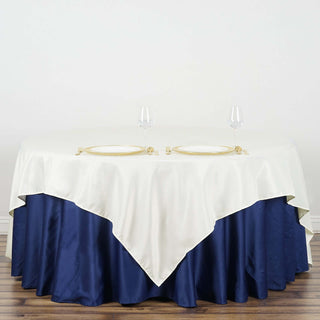 Elegant table setting with cream and navy tablecloth, gold plates, and wine glasses.
