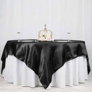 Elegant black satin tablecloth on a white table with decorative crown and flowers.