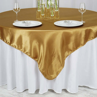 Gold satin tablecloth draped over a white table with plates and glasses.