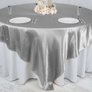 Elegant silver satin tablecloth draped over a round table setting.
