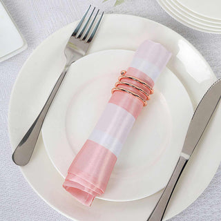 Pink and white striped napkin with rose gold napkin rings on a white plate.
