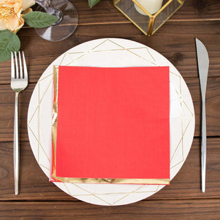 Red napkin with gold trim on a decorative plate, set on a wooden table.