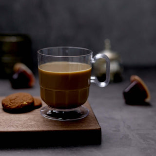 Clear glass mug with coffee and cookies on a wooden surface.