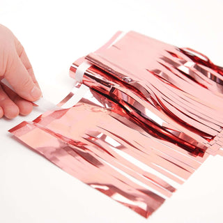 Hand holding shiny rose gold fringe decoration on a white background.