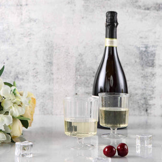 Champagne bottle with two glasses, ice cubes, and cherries on a textured background.