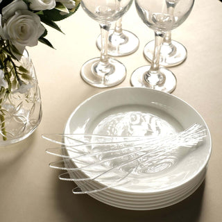 Elegant white dinner plates with decorative skewers and glassware on a neutral table setting.