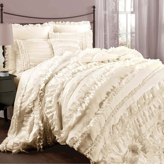 Cream ruffled bedding set on a bed with decorative pillows.
