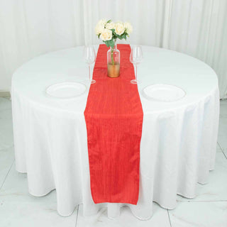 Red table runner on a round dining table set with plates and glasses.