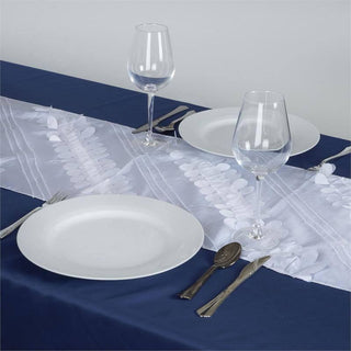 Elegant white table runner on a navy tablecloth with plates and glasses.