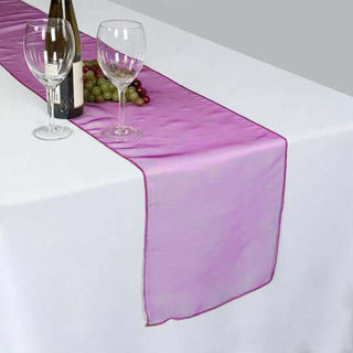 Purple table runner with wine glasses and grapes on a white table.